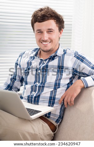 Cheerful man sitting on the sofa and using laptop