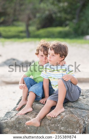 Two hugging little brothers sitting on the beach
