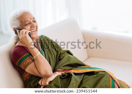 Laughing Indian woman with a telephone sitting on the sofa