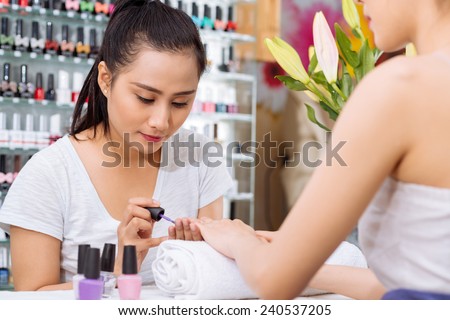 Pretty Asian manicurist applying nail polish