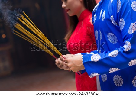 Cropped image of man and woman in ao dai dresses holding incense sticks