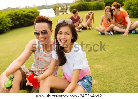 Vietnamese young couple sitting on the grass and drinking beer at the party