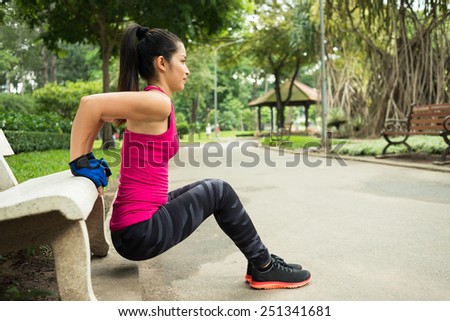 Young woman doing triceps bench dips in the park, side view