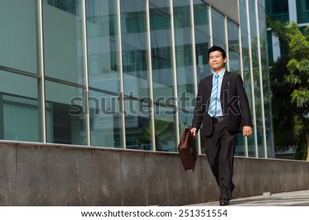 Happy Asian businessman walking along the street