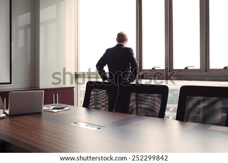 Businessman looking through the office window, rear view