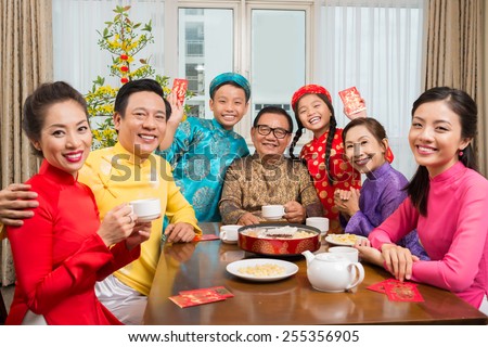 Happy big Vietnamese family in traditional costumes sitting at table and looking at the camera