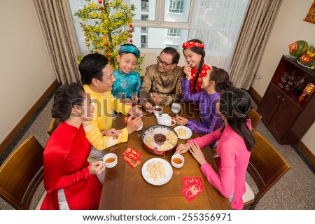 Big Vietnamese family in traditional costumes drinking tea and eating sweets, view from above