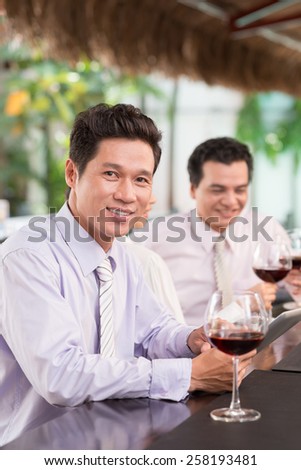 Asian businessman drinking wine and using digital tablet in the bar