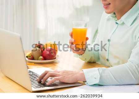 Man drinking juice while working at laptop