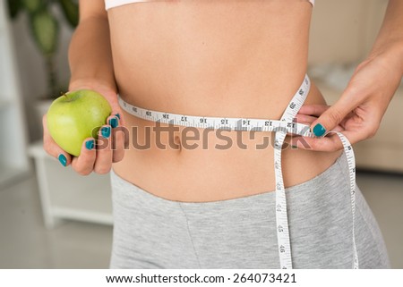 Close-up of woman with green apple measuring waist: healthy lifestyle concept