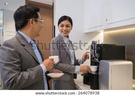 Vietnamese businessman flirting with his female colleague who is making coffee