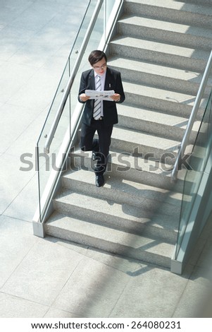 Businessman reading newspaper and going down the stairs