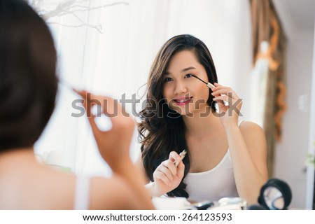 Vietnamese young girl applying mascara in front big mirror