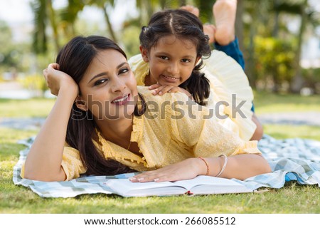 Joyful Indian mother and daughter lying on grass in the park