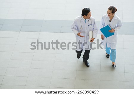 Male and female physicians talking while walking in the hospital, view from above