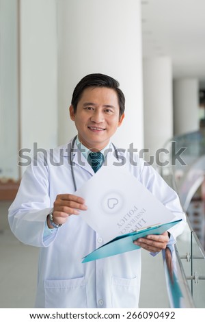 Portrait of smiling Asian doctor with life insurance policy in his hands