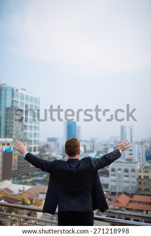 Rear view of powerful businessman raising arms and looking at the city from the rooftop