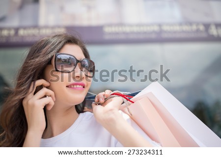 Portrait of beautiful lady in sunglasses holding shopping bags and calling on the phone