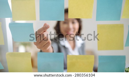 Office worker taking stick note from the wall, focus on hand