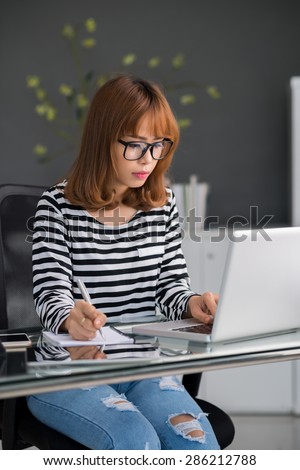 Attractive young woman looking at computer screen and copying out information
