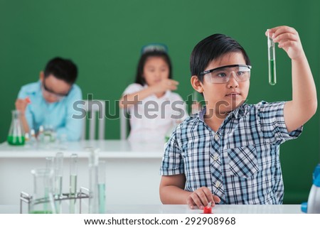 Vietnamese schoolboy in goggles looking at the test tube in his hand