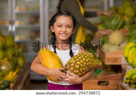Portrait of happy Indian girl with pineapple and melon in her hands