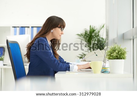 Side view of concentrated business lady working on laptop at the table