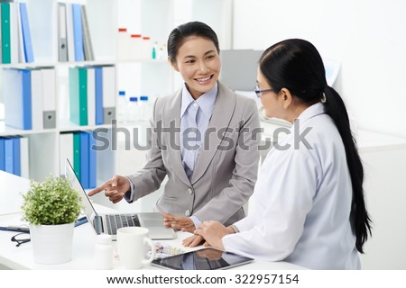 Cheerful Asian business lady using laptop at meeting with medical scientist