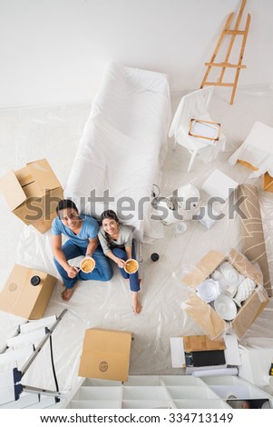 Cheerful Asian couple looking at the camera when eating in their new house, view from the top
