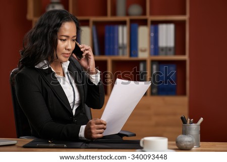 Female Asian lawyer reading contract and consulting client on the phone