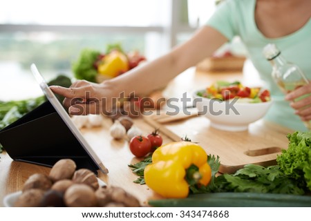 Woman checking recipe on digital tablet before seasoning salad