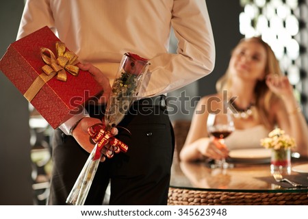 Man hiding red rose and gift for his girlfriend behind his back