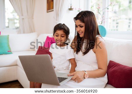 Indian woman and her little daughter watching cartoons on laptop