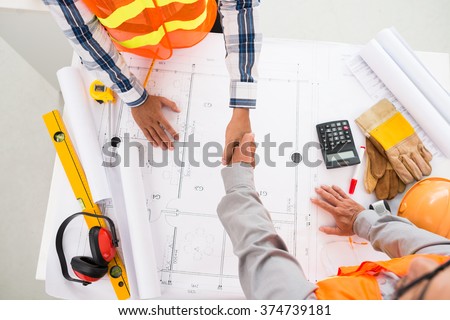Contractor and engineer shaking hands over blueprint of building