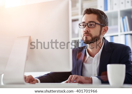 Young businessman in glasses working on computer in office