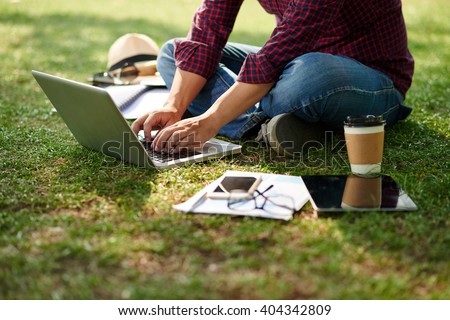 Cropped image of student sitting on the ground and working on laptop