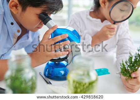 Close-up image of pupils examining plants with microscope and magnifying glass