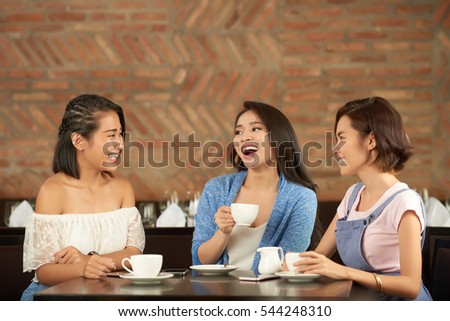 Asian female friends laughing when chatting in cafe