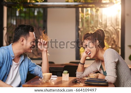 Side view portrait of laughing Asian couple enjoying date in cafe