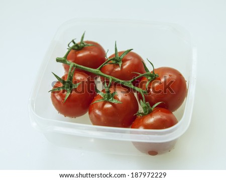 Branch of cherry tomatoes with drops of water in a transparent plastic container