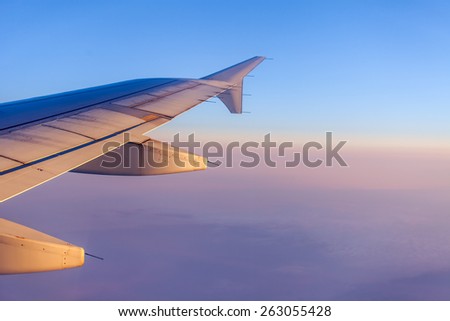 Flight at sunrise. The wing of the plane and the sky lit with beams of a rising sun. Plane view from the window