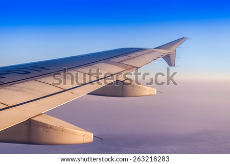Flight at sunrise. The wing of the plane and the sky lit with beams of a rising sun. Plane view from the window