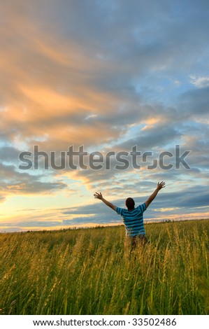young man rising hands over sunset