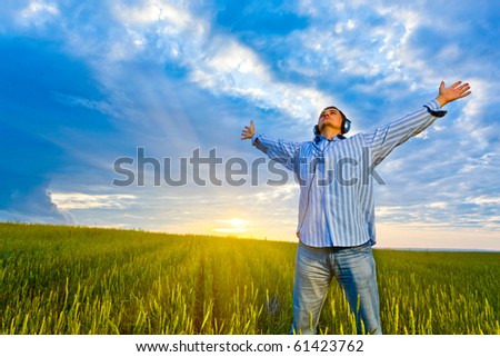 man with headphones standing on field before sunset