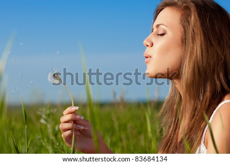 beautiful woman blowing to dandelion on green field