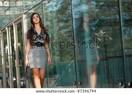 woman walking along glass wall and holding bag