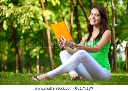 brunette woman reading book at green summer park