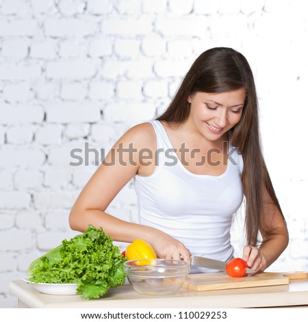 brunette woman cutting  fresh tomato over white brick wall