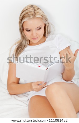 beautiful blonde woman reading book in bed