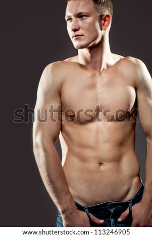 Handsome macho man posing shirtless to display his physique and muscles , upper body portrait on a dark studio background